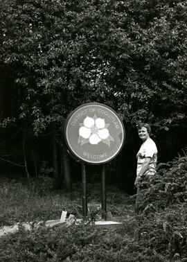 Person standing next to the City of Coquitlam dogwood welcome sign