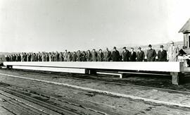 Men and women lined up behind a long timber mast at Fraser Mills