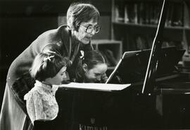 A woman teaching two young girls piano