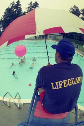 Kids play with a giant ball in a swimming pool while lifeguard watches