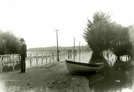 Man with rowboat at main fence during flood (Colony Farm)