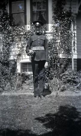 Man in military uniform holding a bugle in front of likely Essondale Cottage 118