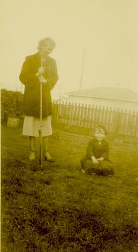 Woman raking with a small boy sitting on the lawn
