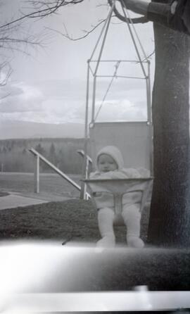 Ida May Headridge holding a baby in a swing