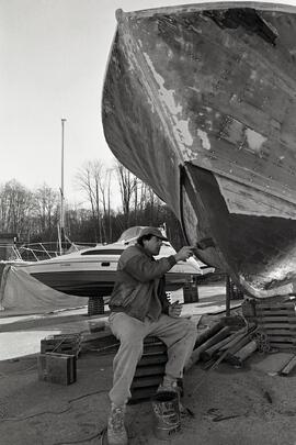 Kevin Heneghan paints the bow of his boat which is under going restoration at Reed Point Marina in Port Moody.