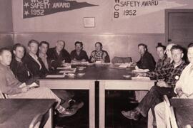Men sitting around a table with WCB Safety Award 1952 pennants on the wall