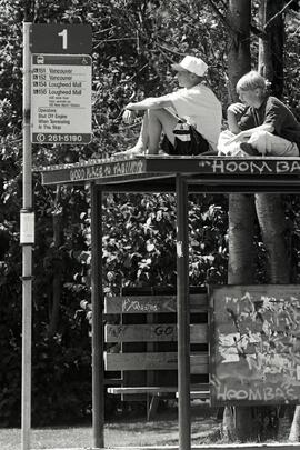 Alex Prittonen and Wes Thomson sitting on top of the bus shelter at King Albert Avenue and Poirier Street