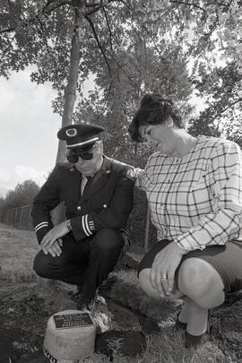 Coquitlam fire captain and Beth MacDonald sitting next to the memorial plaque dedicated to John MacDonald on Chilko Drive