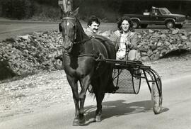 Woman driving horse drawn cart with man inside