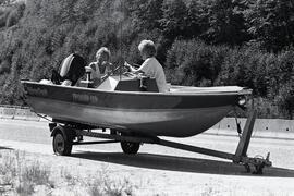 Two women sitting in a twelve foot boat in a towing rig with a blown out tire on Coquihalla Highway