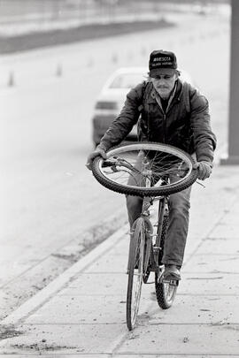 Tour shot of David Wheeler on a bike with a bicycle wheel on the steering wheel on Pinetree