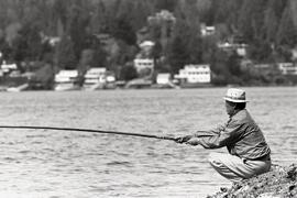 Old [Asian man] fishing from rocks at Belcarra Park, with Deep Cove and Indian Arm in background